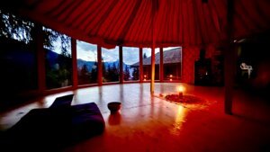 L'intérieur d'une yourte à la tombée de la nuit avec une bougie allumée au centre et vue sur les montagnes et sapins pour une retraite en Suisse.
